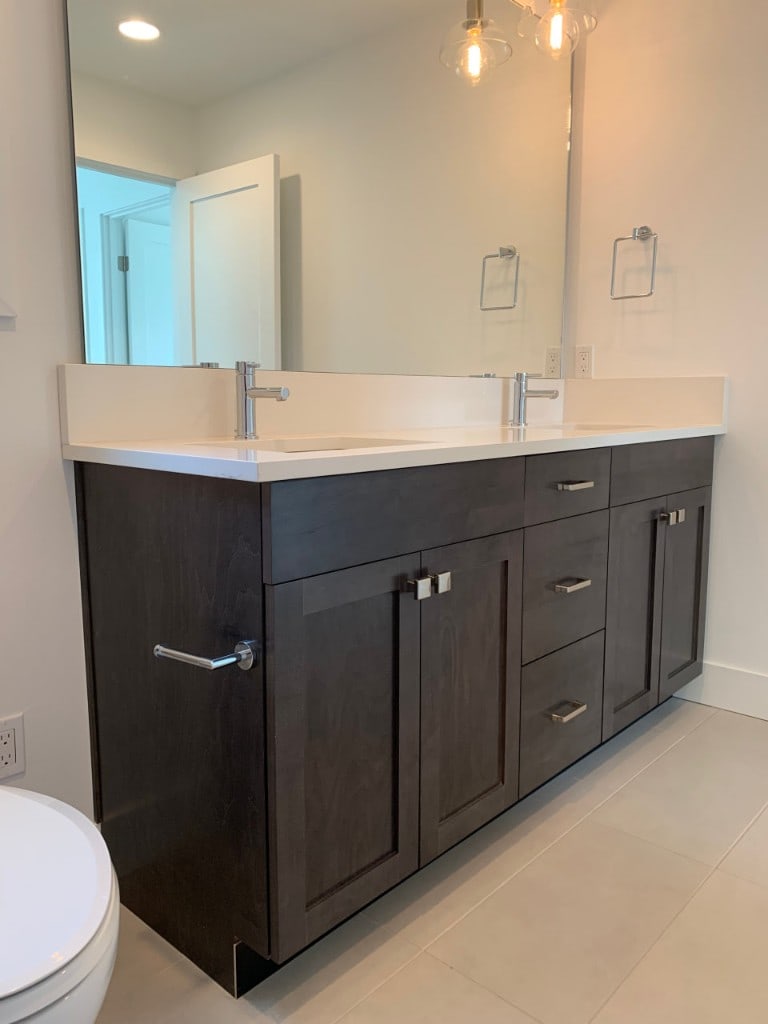 Bathroom with an espresso double vanity, white quartz countertop, and large mirror by Artbrick
