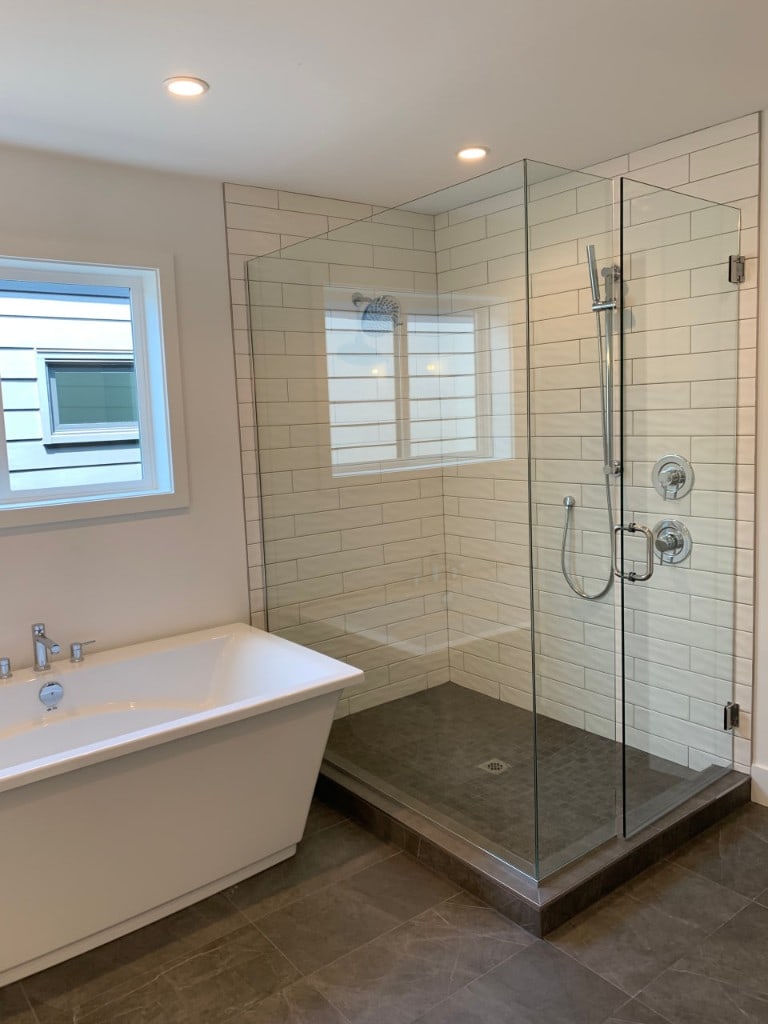 Bathroom with a freestanding soaking tub and glass shower with white subway tile by Artbrick