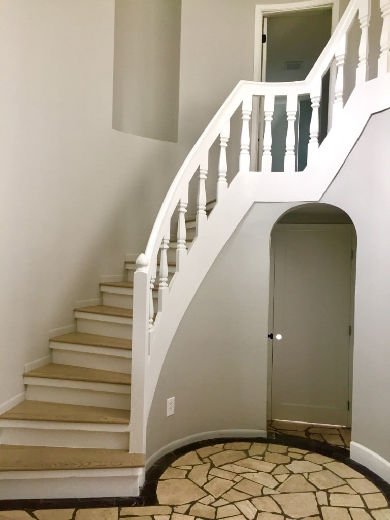 Curved staircase with turned balusters above a stone-tile entry after renovation by Artbrick