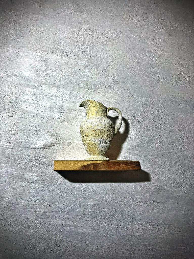 Textured decorative plaster pitcher spotlit on a wood shelf against a plaster feature wall by Artbrick