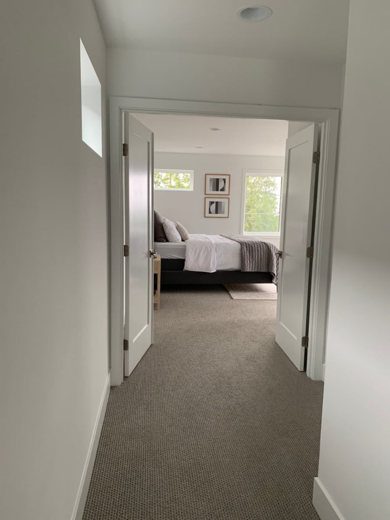 Carpeted hallway with double doors opening into a renovated master bedroom by Artbrick