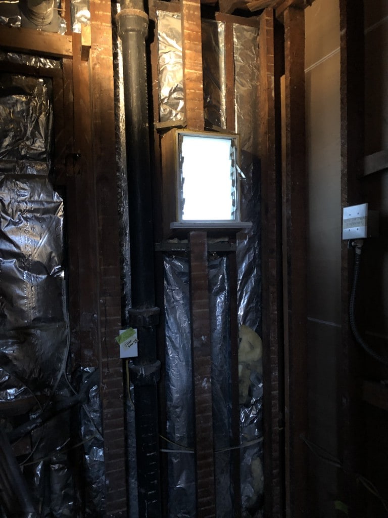 Open wall cavity with foil-faced insulation during interior demolition by Artbrick