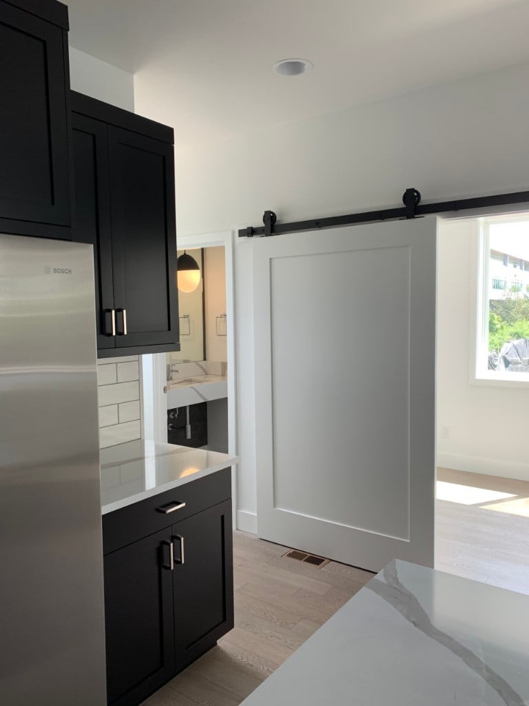 Renovated kitchen with black shaker cabinets, quartz counters, and a sliding barn door by Artbrick