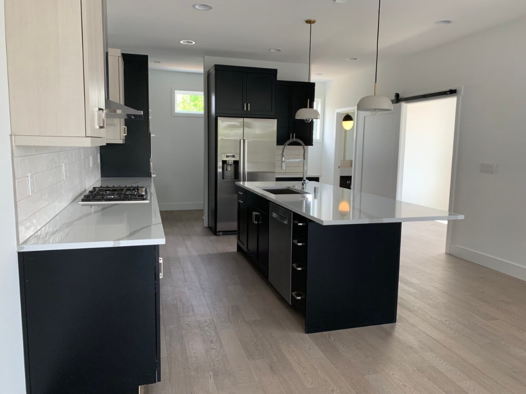 Remodeled kitchen with black cabinets, a white quartz island, and subway tile backsplash by Artbrick
