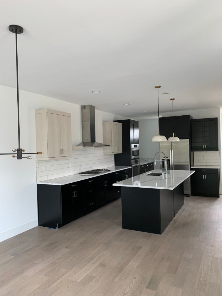 Two-tone kitchen remodel with black and light cabinets, an island, and a stainless range hood by Artbrick