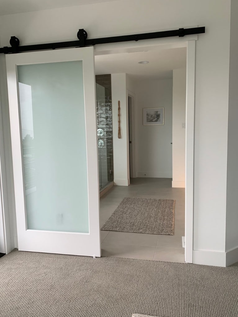 Master bedroom with a frosted barn door opening to a tiled ensuite bathroom by Artbrick
