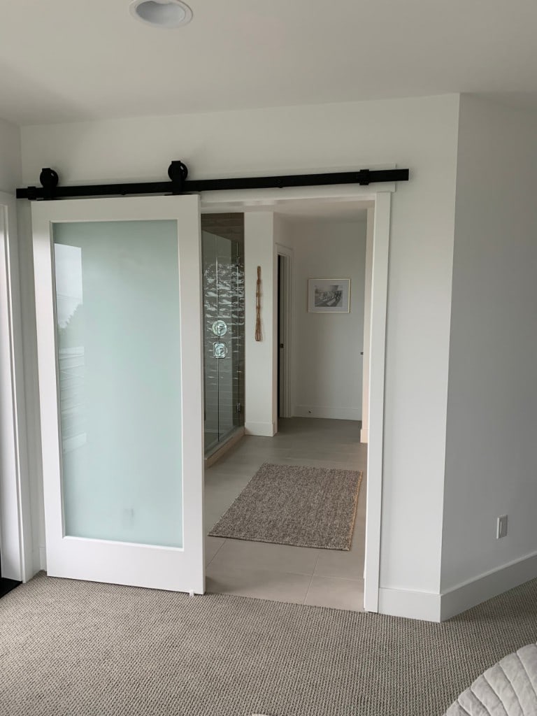 Master suite with a frosted-glass barn door leading to a tiled ensuite bathroom by Artbrick