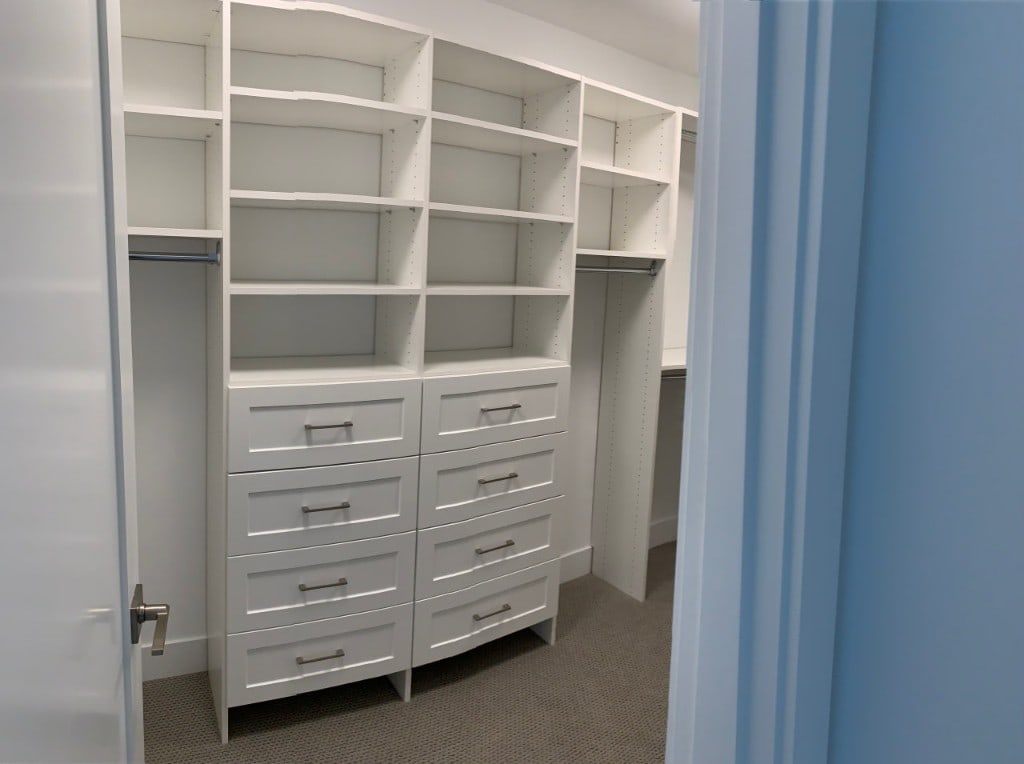 Walk-in closet with built-in white shelving and a bank of drawers by Artbrick